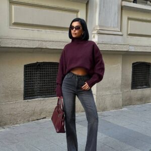 Model in einem crop burgunderroten Rollkragenpullover, hoch taillierte ausgewaschene schwarze Jeans mit dezenten Nieten, burgunderrote Tasche und spitze Absätze. - Großhandel Türkei verfügbar