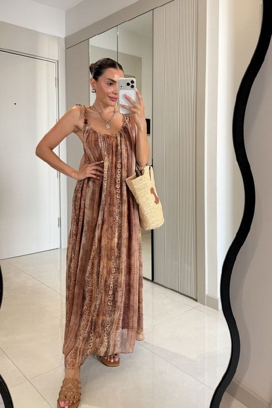 angled-front-tie-dress-7391 Angled front view of brown patterned tie-shoulder maxi dress, flowing skirt, woven tote and sandals. available for wholesale in Turkey.