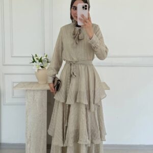 Front view highlighting bow neck detail, cinched waist and cascading layered skirt in beige crinkle fabric. Wholesale Turkey.