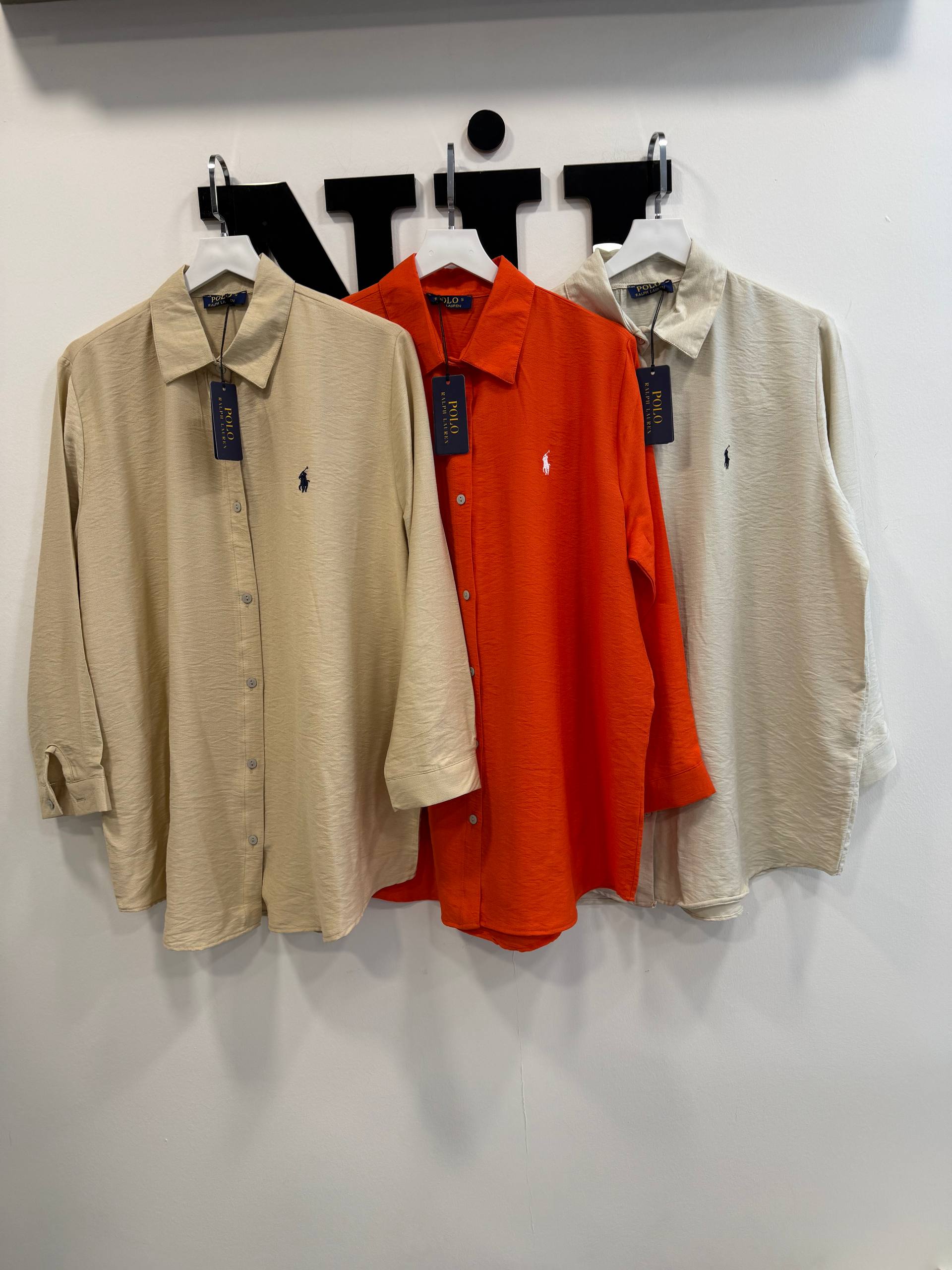 beige-orange-trio-4821 Three longline textured button shirts on hangers in beige, bright orange and pale beige, showing collars and chest embroidery. available for wholesale in Turkey.