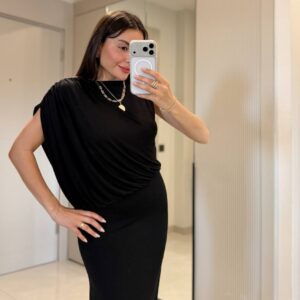 Close-up mirror selfie of black draped top with asymmetrical sleeve and soft jersey drape over a slim skirt.