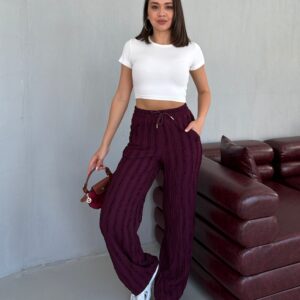 Model hält eine black Canvas-Tasche mit weißem Frontdruck neben texturierten schwarzen Hosen und Crop-Top.