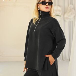 Acercamiento del top de velour negro con cremallera en media altura y cuello alto; la modelo lleva gafas de sol y pendientes de aro dorados.