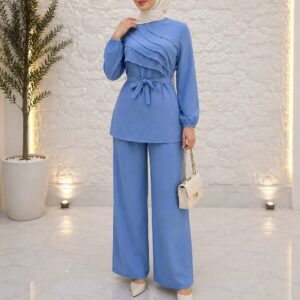 Model wearing sky-blue textured tunic with layered diagonal panels, tied waist belt and matching wide-leg trousers.