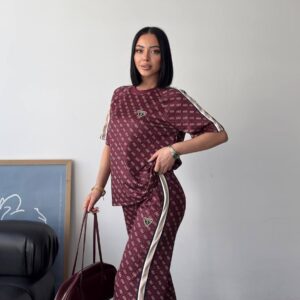 Side view of burgundy monogram two-piece featuring cream striped piping and flared leg, model holding bag.