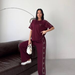 Model wearing a burgundy tee and wide-leg trousers featuring stitched side motifs and an elastic waist, styled with white sneakers.