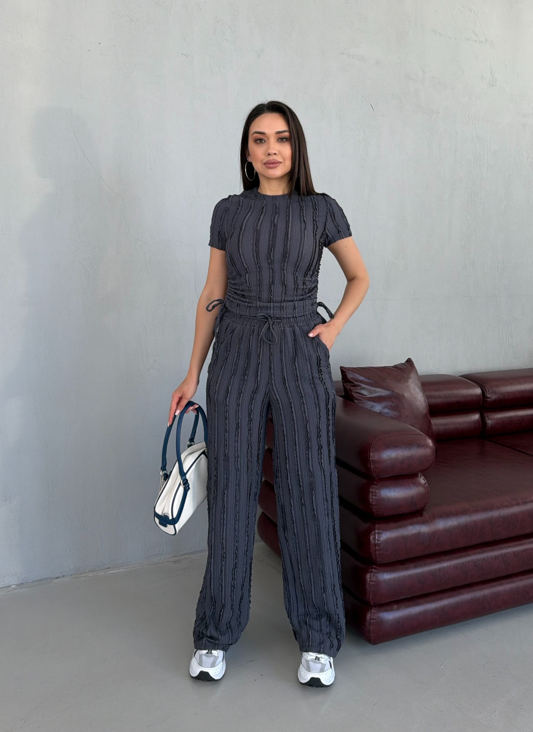 anthrazit-texturierter-jumpsuit-4821 - Großhandel Türkei Ganzkörperansicht eines anthrazitfarbenen texturierten Zwei-Teile-Sets mit kurzärmligem Oberteil, weiter Hose und weißen Sneakern. Großhandel Türkei erhältlich.