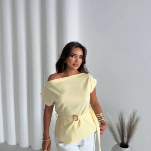 Blusa asimétrica color amarillo pálido con cinturón de aro dorado, combinada con pantalones blancos y clutch dorado. - Mayorista en Turquía