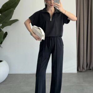 Two-piece black lounge set: short-sleeve zip-collar top and wide-leg drawstring pants, paired with white sneakers and clutch.
