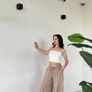 Model in white strapless bandeau and high-waist beige wide-leg drawstring pants, cinched ankles, white heels.