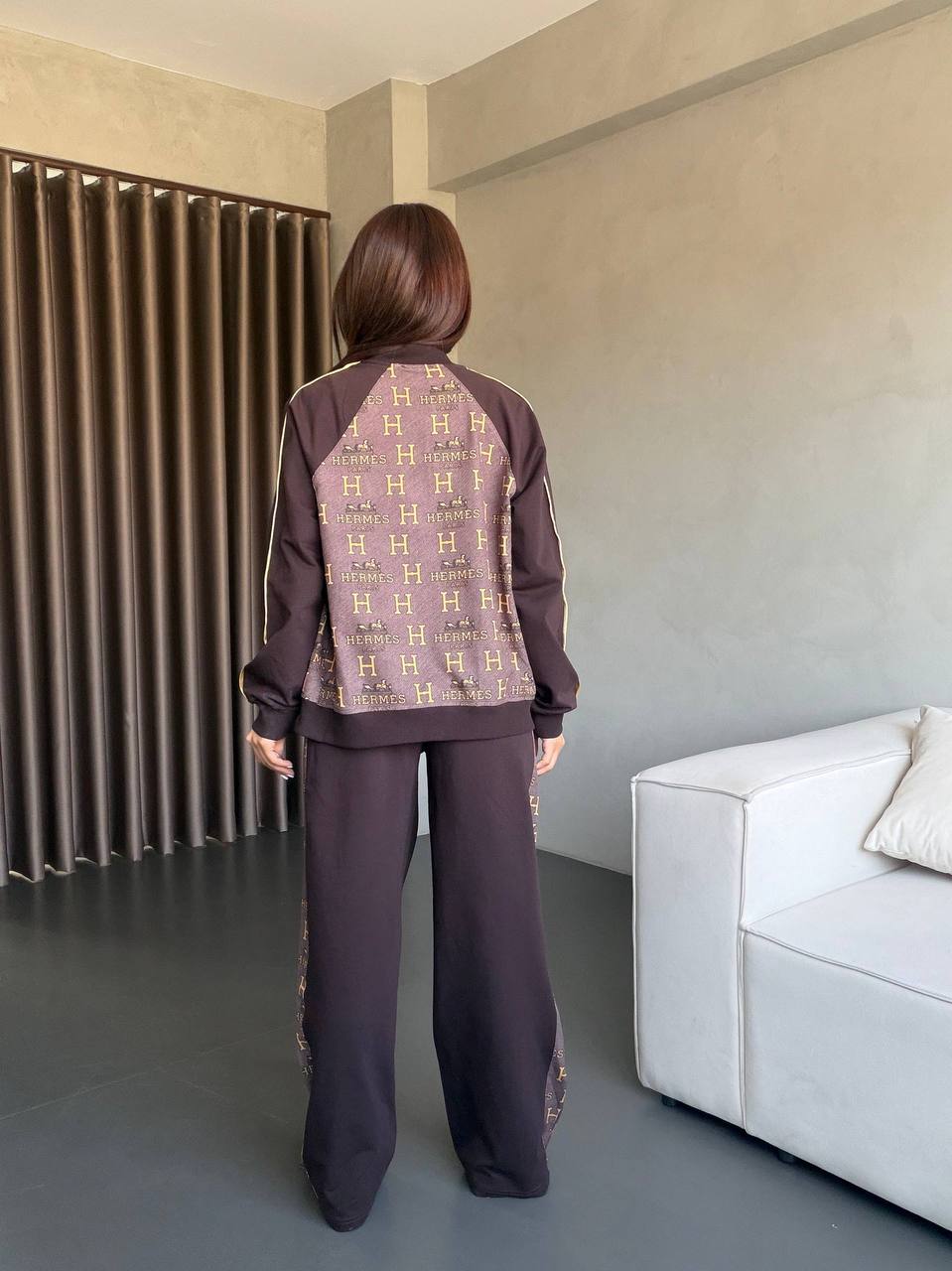 Back view of dark brown two-piece tracksuit with monogram-print back panel, piped sleeves, and wide-leg pants. Back view of dark brown two-piece tracksuit with monogram-print back panel, piped sleeves, and wide-leg pants.