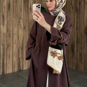 Plano medio de una abaya granate que destaca un pañuelo de seda crema con patrón y un bolso bandolera pequeño con detalles en cuero marrón. - Turquía Mayorista