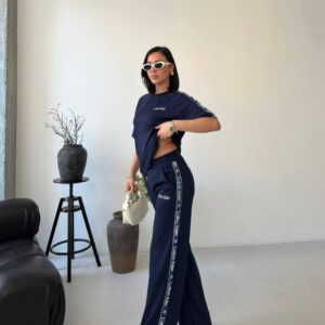 Standing model in navy top and wide-leg trousers featuring contrast logo tape along the outer seam.