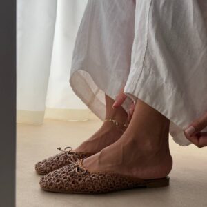 لقطة بسيطة على القدم لصندل منسوج واحد يرتدى مع تنورة كتانية بيضاء، اليد تمسك الكعب وتظهر أصابع مطلية.