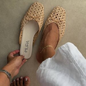 Angled top view of one mule worn, showing open-back design, woven raffia crochet upper and cream cushioned insole.