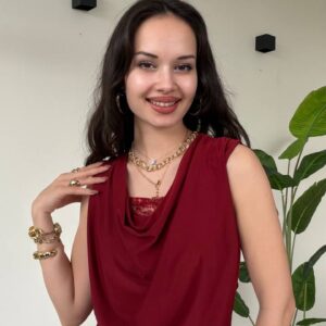 Vista frontal de la blusa drapeada en red, superpuesta a una camisola de encaje roja y pantalones beige.