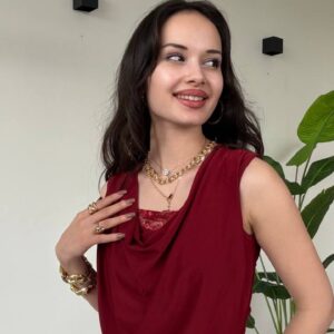Vista de tres cuartos de la blusa drapeada en red, mostrando pliegues laterales, ajuste relajado y detalle de pulsera dorada.
