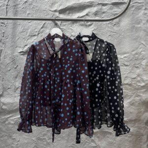 Vista desde arriba que destaca la cintura fruncida, la tapeta de botones y mangas acampanadas en blusa de lunares de chiffon. Mayorista Turquía.