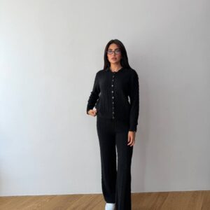 Front view of model in black cable-knit button-up cardigan and matching wide-leg pants, wearing white sneakers and glasses.