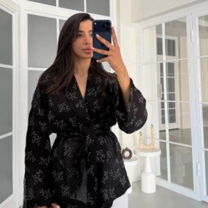 Mirror selfie showing black sheer kimono with tonal floral print, wide sleeves and tied waist over white shorts. available for wholesale in Turkey.