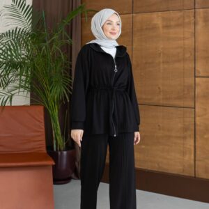 Vollständiges Bild der schwarzen Reißverschluss-Jacke mit weiter Hose, hellgrauem Hijab und weißen Sneakern.