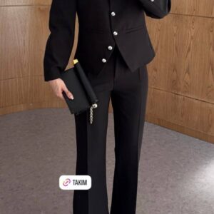 Mid-shot of black jacket front showing stand collar, round silver buttons, welt pockets, cuff buttons and fitted trousers.