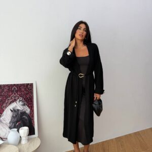 Cárdigan negro midi atado con cinturón delgado y herraje dorado, puños enrollados con botón decorativo, sobre vestido negro tipo slip - Mayorista Turco