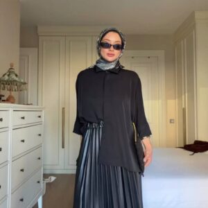 Modelo con falda plisada negra de cintura alta, tunica negra suelta, pañuelo estampado y gafas de sol - Mayorista en Turquía.
