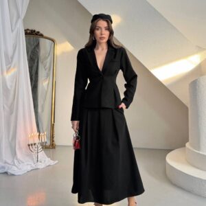 Vista frontal de blazer negro de un solo botón con cintura ceñida y falda larga a juego, con tacones rojos y bolso pequeño. - Mayorista Turquía