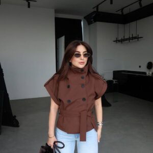 Full-body front view of brown double-breasted belted top with high funnel collar and black buttons, styled with light jeans and braided tote. available for wholesale in Turkey.