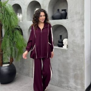 Modelo caminando con chaqueta burgundy con cremallera y dobladillo elástico, bolsillos delanteros, combinada con pantalones de pierna ancha burgundy y raya lateral crema.