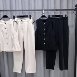 Two sleeveless button-front tops with pleated hems and matching trousers on a clothing rack; cream and black colorways.