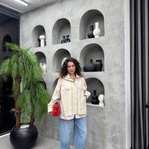 Modelo con chaqueta crema de gran tamaño con cremallera y broche frontal, sosteniendo un bolso rojo brillante y luciendo denim suelto. - Mayoreo Turquía