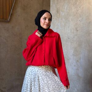 Three-quarter view of cropped red jacket with covered buttons, paired with polka-dot maxi skirt and black hijab.