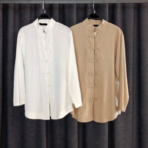 Close-up of two mandarin-collar tunics hanging side by side in white and camel beige, showing textured lightweight fabric.