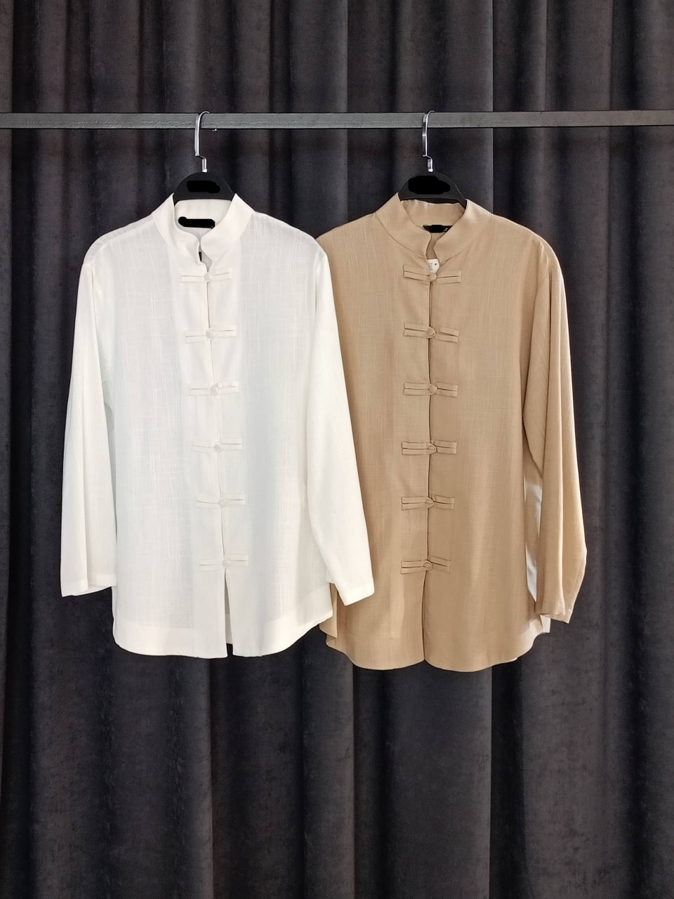 duo-tunic-closeup-7619 Close-up of two mandarin-collar tunics hanging side by side in white and camel beige, showing textured lightweight fabric.
