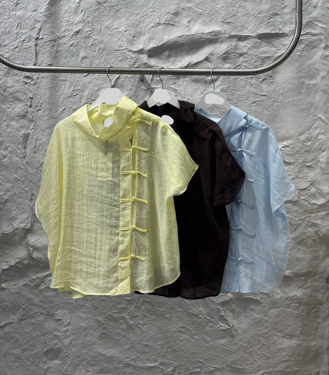 tops-colgados-con-nudo-lino-9574 – Mayorista Turquía Tres tops (amarillo palido, negro, azul claro) colgados en una percha, textura de lino arrugado con cierres verticales de nudo - Mayorista Turquía