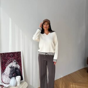 Vollständige Länge eines elfenbeinfarbenen Strick-Pullovers mit gestreiften Bündchen, kombiniert mit schokoladenbrauner Weitehose und brauner Baseballkappe – Türkei-Großhandel.