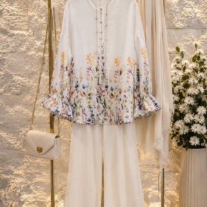 Ivory blouse with multicolor floral hem print, pearl-button placket and ruffled sleeve cuffs, styled with cream pants.