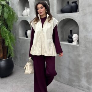 Vorderansicht einer elfenbeinfarbenen Zip-Weste über burgundfarbener Wide-Leg-Hose-Kombination, cremefarbene quilted Handtasche.