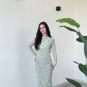 Full-length mint midi dress with diagonal drape, sheer dotted sleeves and white pointed heels.