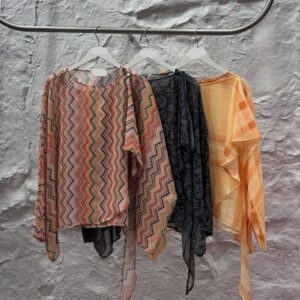 Tres blusas translúcidas de manga larga en perchas con estampados en zigzag, paisley oscuro y cuadros naranja, con lazos drapeados en los costados - Mayorista Turquia.