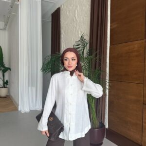 Three-quarter view of woman wearing a textured white tunic with frog-style knot closures, brown hijab and dark clutch bag. available for wholesale in Turkey.