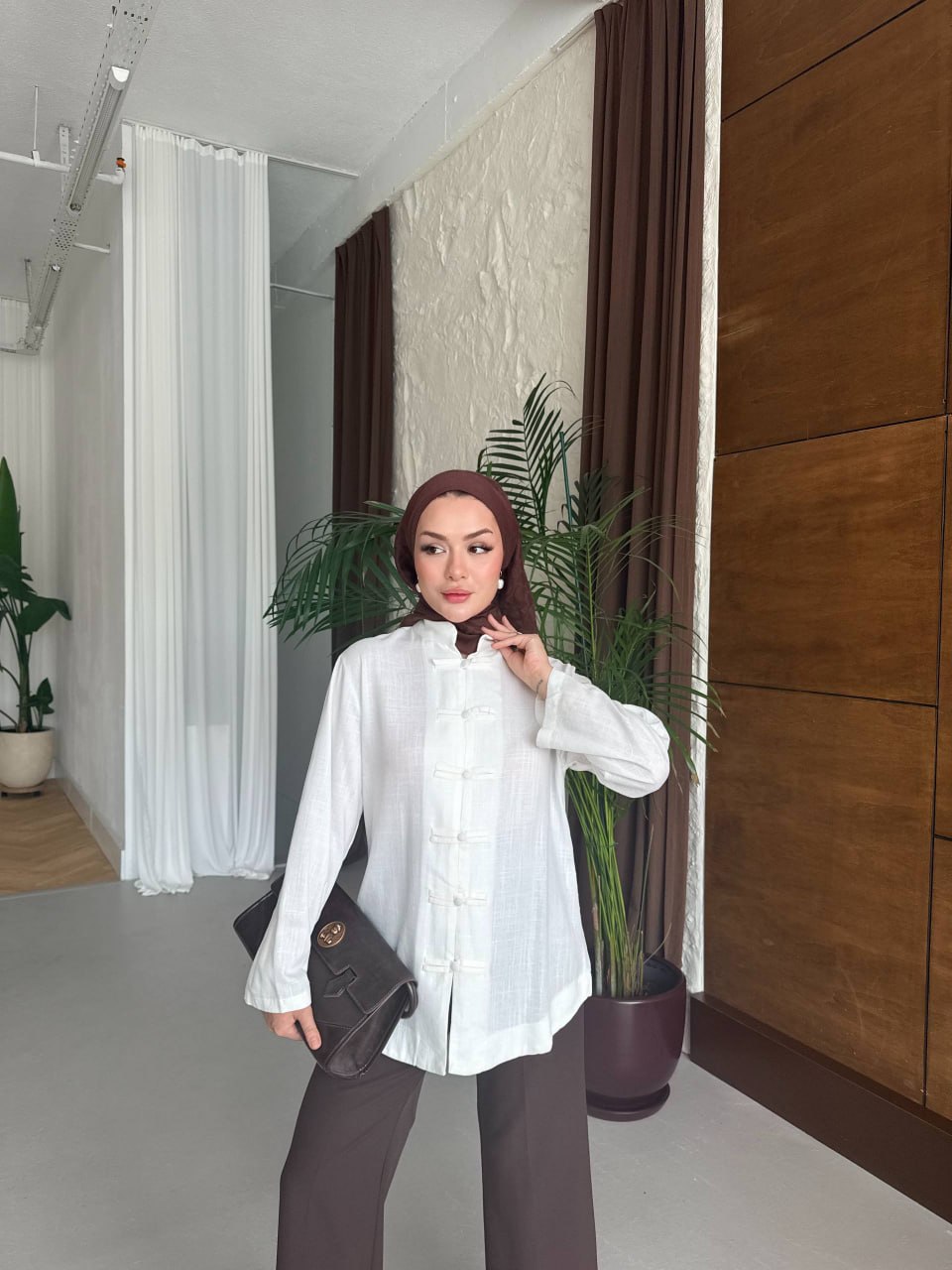 model-tunic-closeup-8361 Three-quarter view of woman wearing a textured white tunic with frog-style knot closures, brown hijab and dark clutch bag. available for wholesale in Turkey.