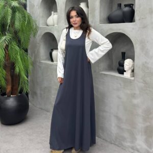 فستان ماكسي طويل بلا أكمام باللون الأزرق الكحلي العميق مُرتدى فوق قميص داخلي أبيض؛ قماش خفيف وتقليم A-line فضفاض.