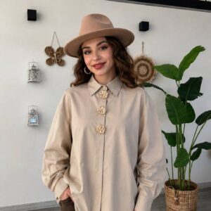 Front view of oversized beige shirt with three decorative gold buttons, styled with a tan fedora and brown mini skirt. - B2B Turkiya