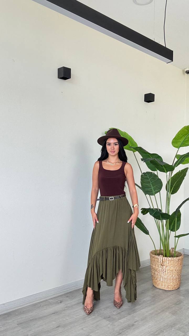 oliva-falda-asimétrica-7621 - Mayorista Turquía Modelo con falda asimétrica oliva de dobladillo alto-bajo con volantes, top marrón sin mangas y sombrero, tacones con estampado de leopardo junto a una planta en maceta. Disponible para mayoreo en Turquía - Mayorista Turquía.