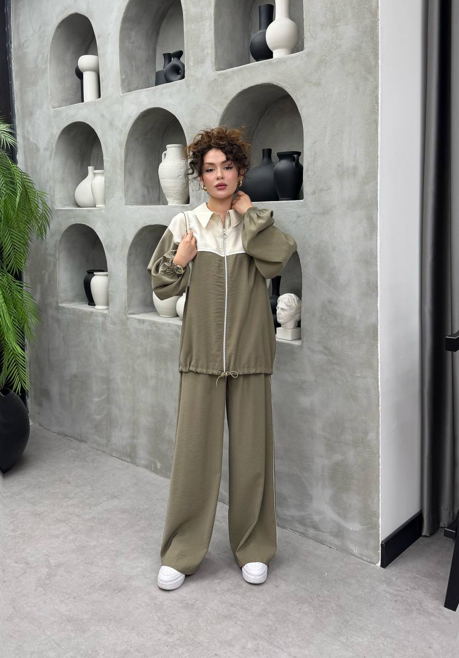 olive-cream-trackset-1047 Model in olive zip jacket featuring cream upper panel and elastic hem, paired with wide, flowing trousers.