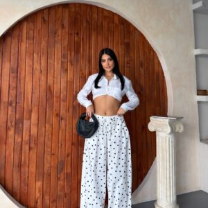 Vorderansicht: Modell trägt weiße Hose mit hohem Bund im Polka-Dot-Muster und kurzes weißes Oberteil, hält eine schwarze Tasche. Großhandel Türkei verfügbar. - Großhandel Türkei
