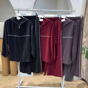 Fila de chaquetas con capucha y cremallera y pantalones con cintura elástica en negro, burdeos y gris apagado con ribetes blancos.